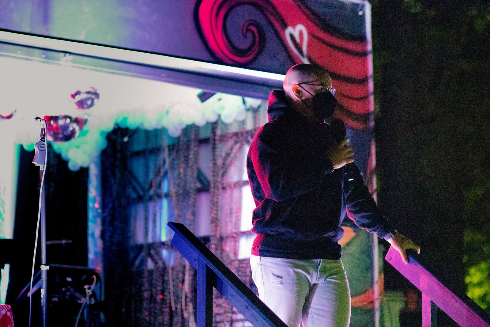 a man wearing a mask speak on a stage with disco balls and pink lights