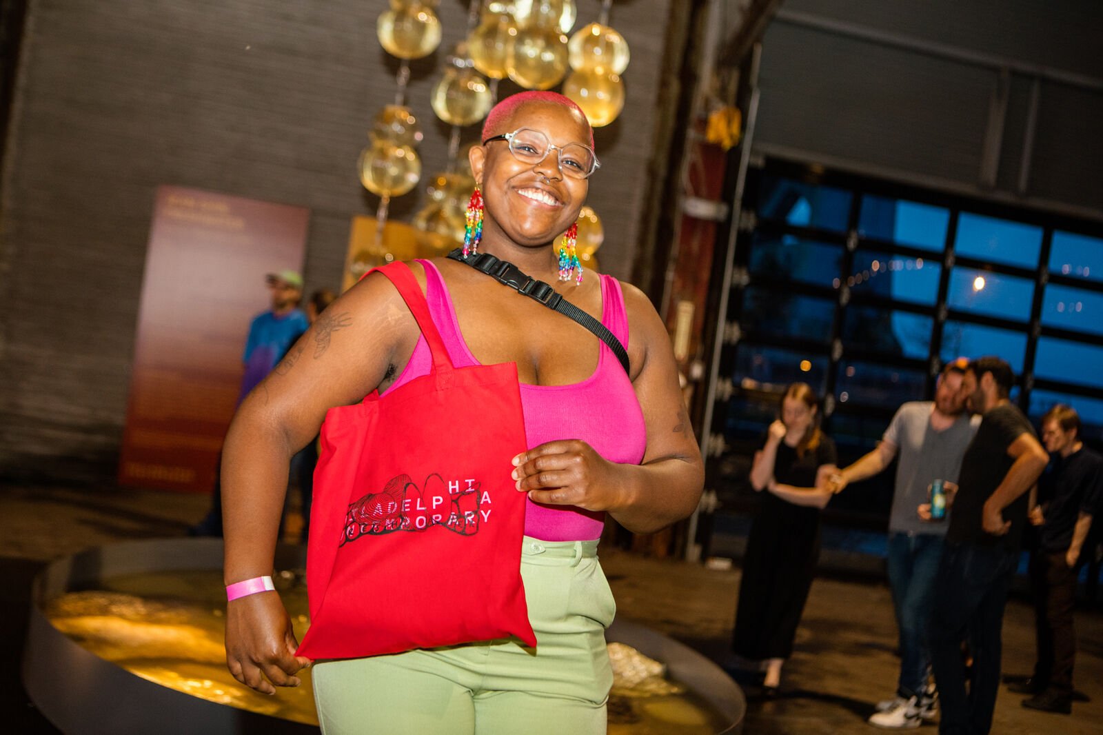 Artist Marian Bailey showcasing a red tote bag with text: Philadelphia Contemporary, and the illustration that she created for the evening's screen-printing activity